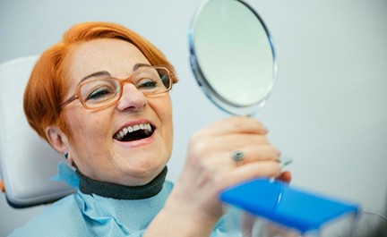 A smiling older woman admiring her dentures in a hand mirror