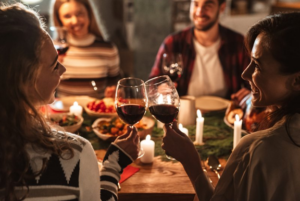 Two friends tapping their red wine glasses together at holiday meal